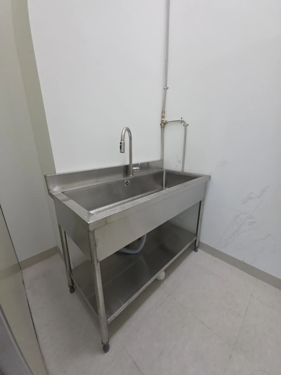 완전히 빈 방 구석에 새로 설치된 코너 단조 개수대와 하부 선반